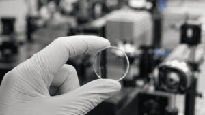 Single clear 5D memory crystal glass storage disc held in gloved fingertips under laboratory lighting
