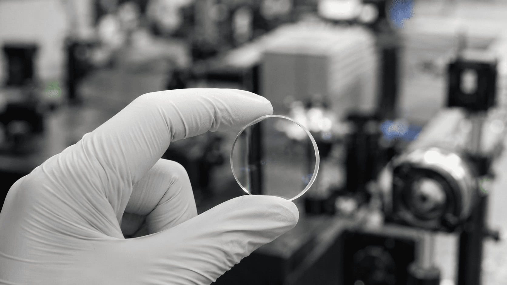Single clear 5D memory crystal glass storage disc held in gloved fingertips under laboratory lighting