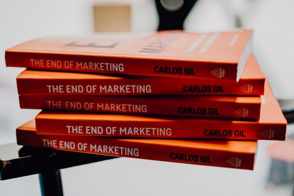Stack of four copies of 'The End of Marketing' by Carlos Gil on a black surface.