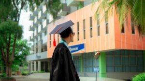 Graduado con toga y birrete de pie frente a un moderno edificio universitario.