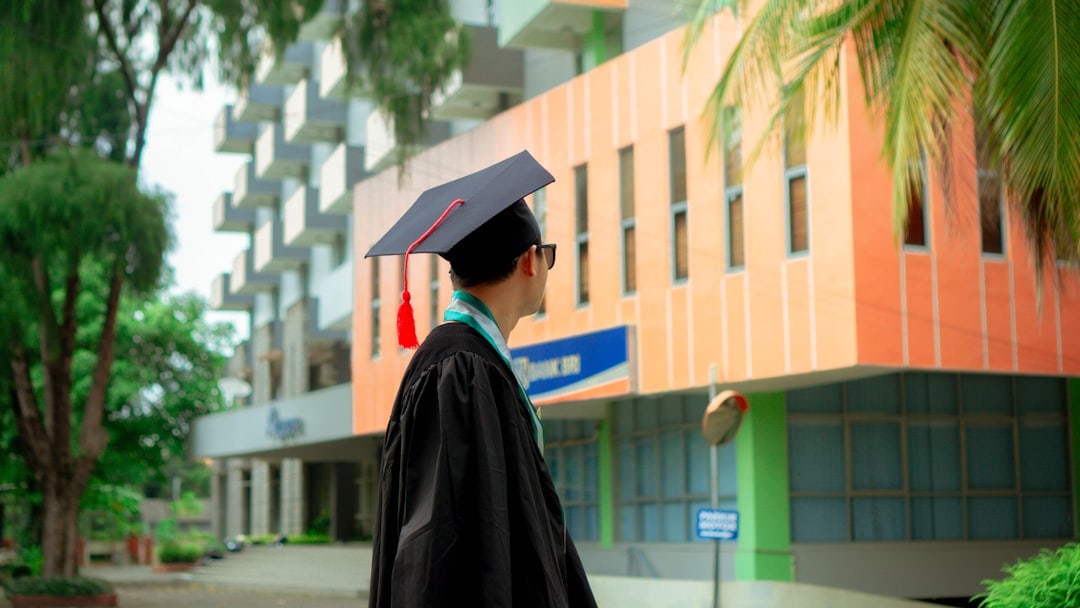 Graduate in cap and gown standing outside modern university building.