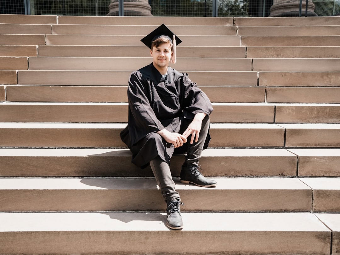 Graduate in cap and gown sitting on steps at graduation ceremony.