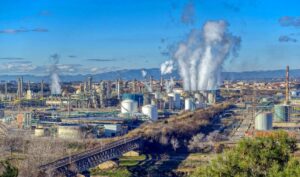 Industrial oil refinery with smoke emissions and pipelines in a large industrial complex.