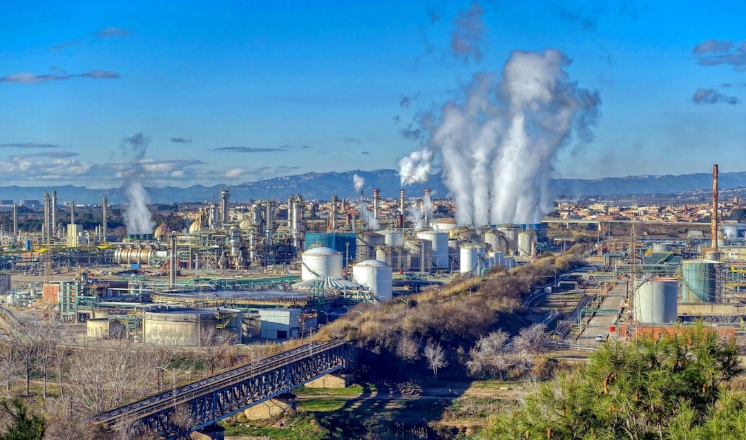 Industrial oil refinery with smoke emissions and pipelines in a large industrial complex.