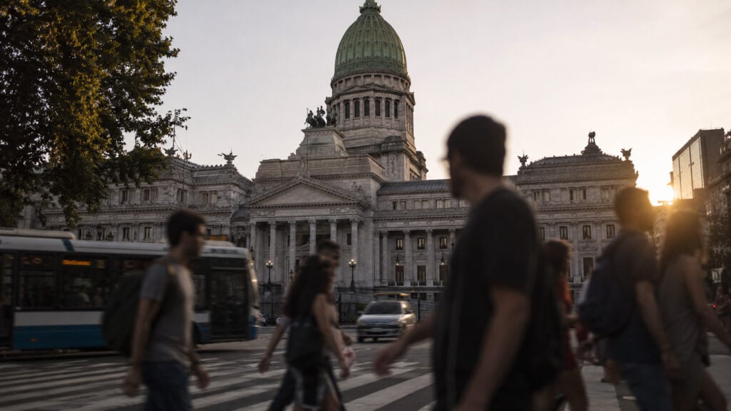 Exterior of the Argentine National Congress building in Buenos Aires with pedestrians crossing in the foreground at golden hour.