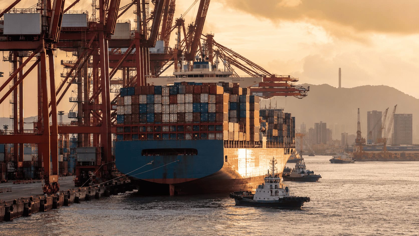 Gantry cranes loading shipping containers onto a cargo ship at a Chinese port at dusk