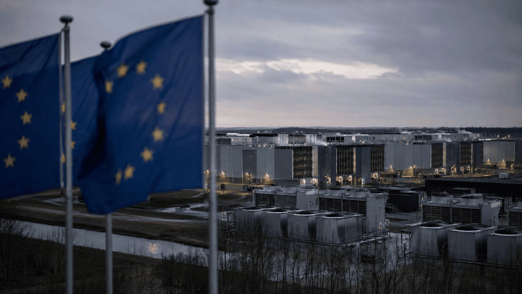 Exterior of a large data center campus in Europe at dusk with EU flags in the foreground.