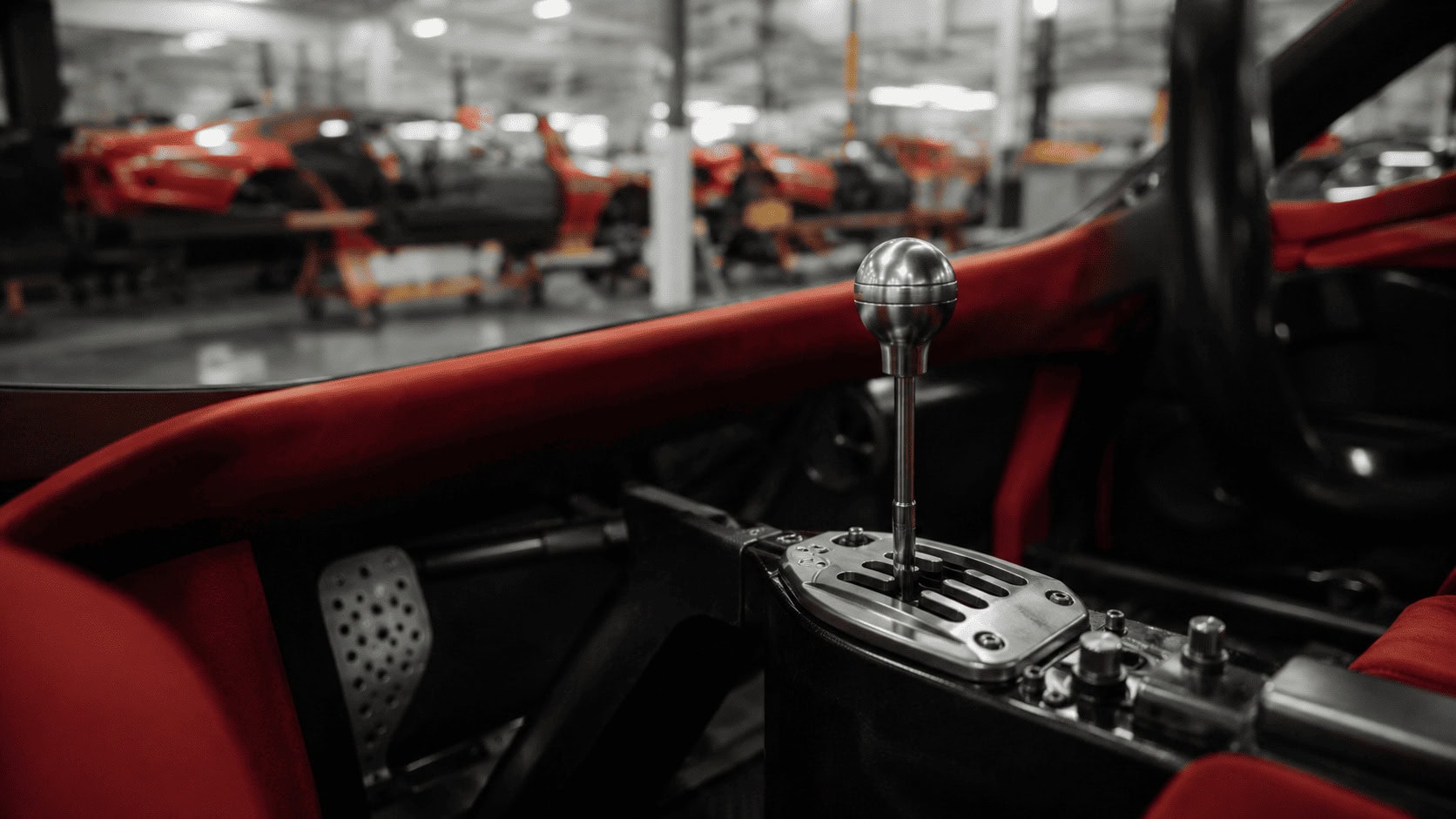 Close-up of an exposed gated manual gear shifter inside a red sports car on an assembly line.