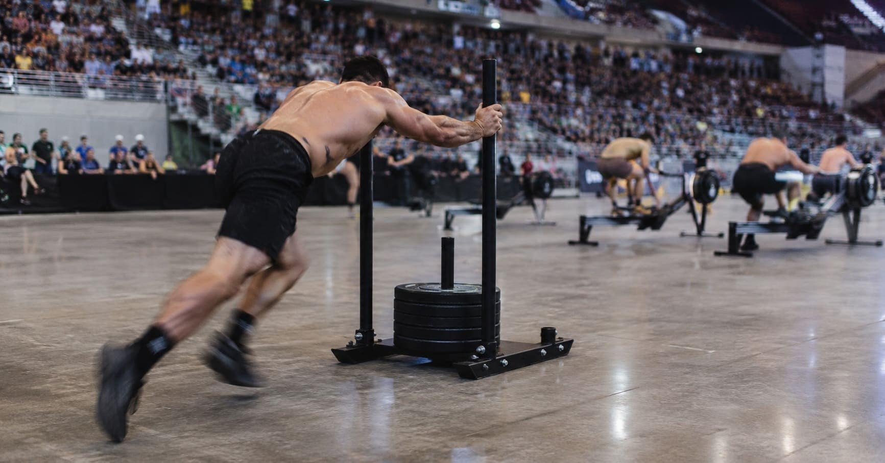 Athlete pushing a weighted sled during an indoor functional fitness race, illustrating the Hyrox business model and event-based revenue.