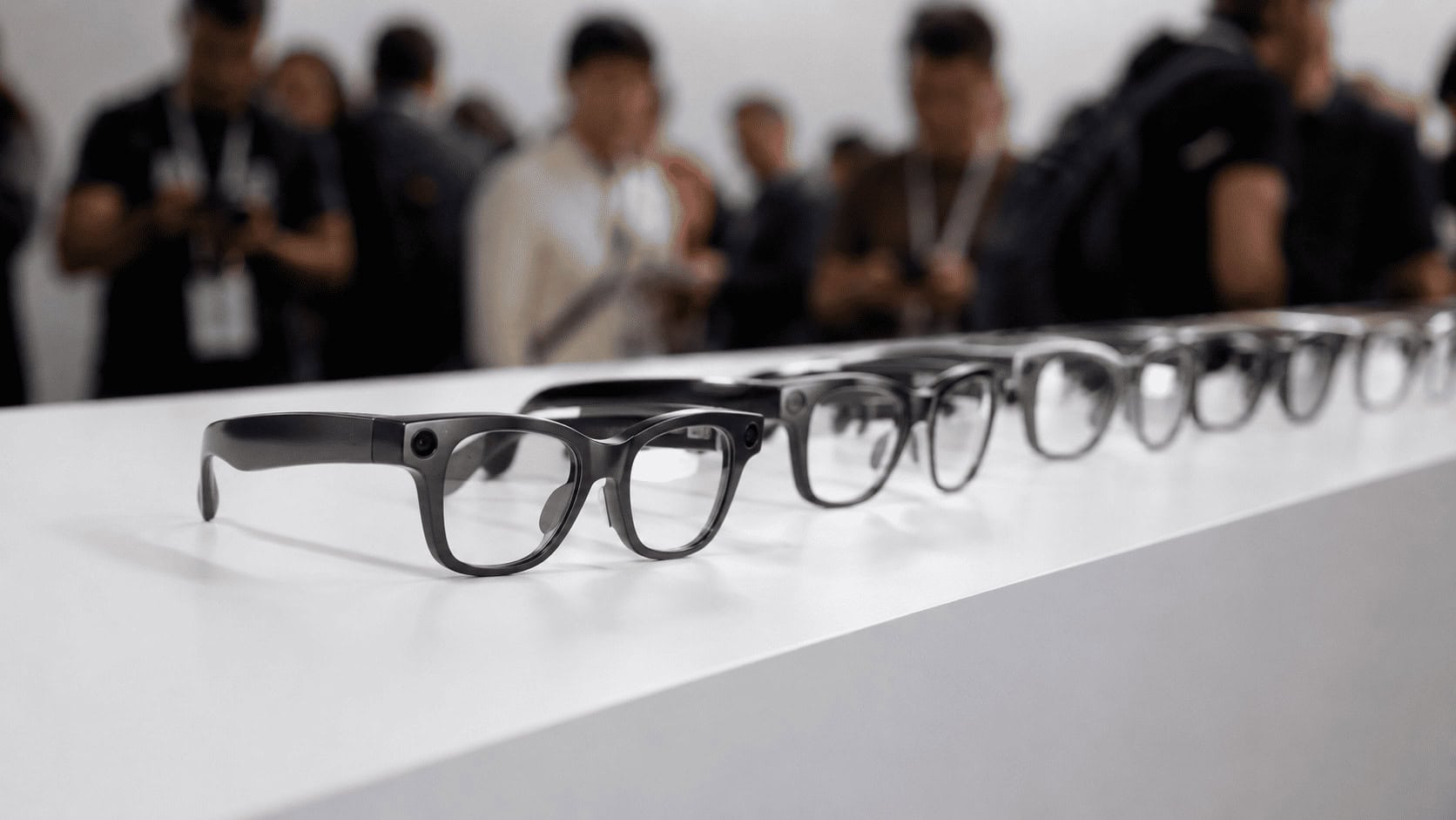 A row of dark and tortoiseshell smart glasses arranged on a white display surface at a product launch event.