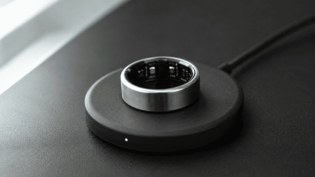 Titanium smart ring resting on a circular wireless charging plate on a charcoal surface