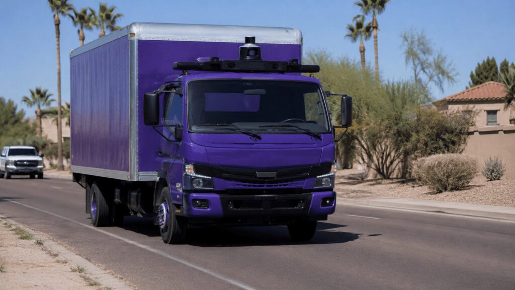 A purple autonomous box delivery truck with a roof-mounted sensor driving on a sunny suburban road lined with desert plants.