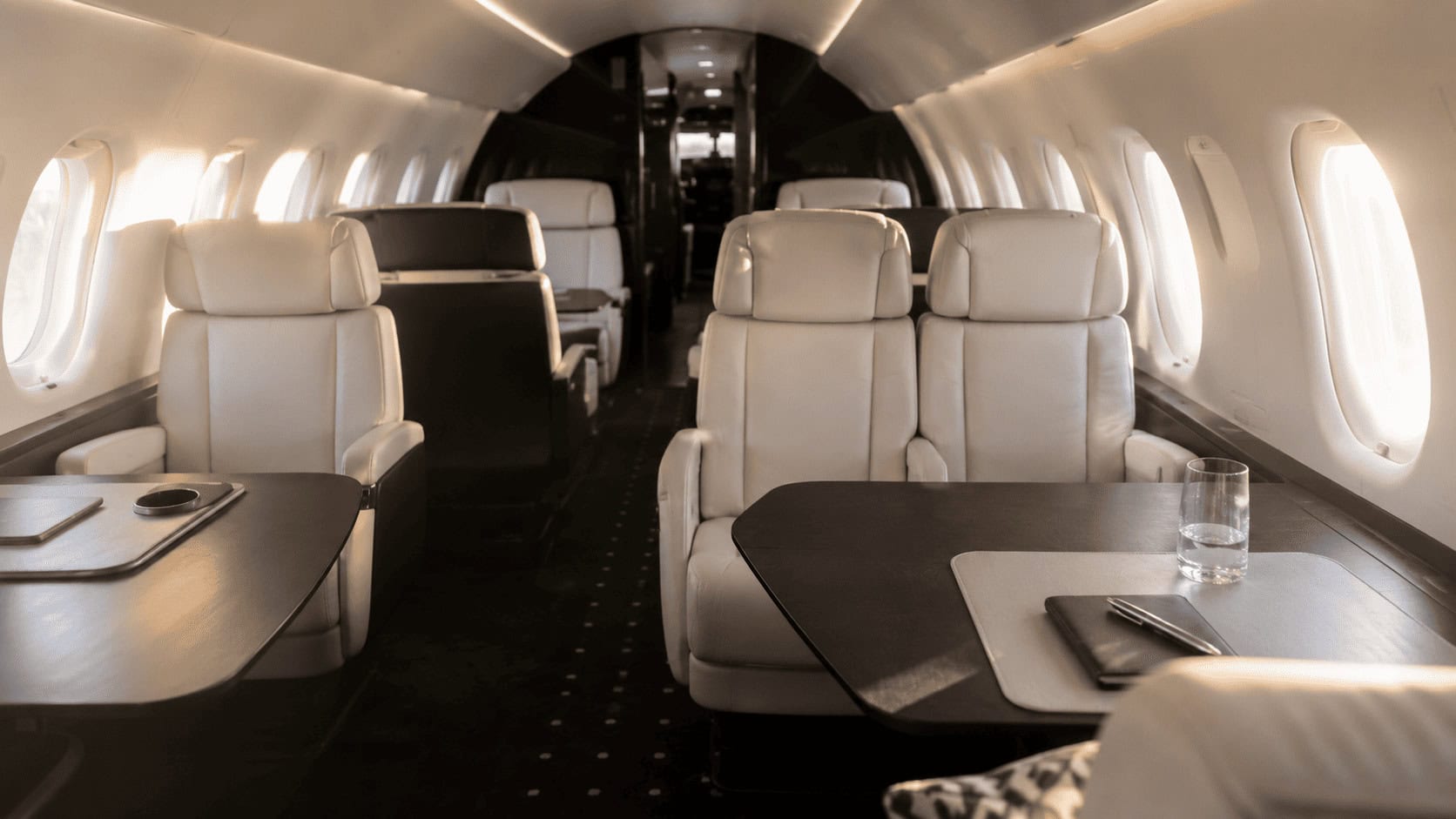 Empty cream leather seats inside a private jet cabin lit by afternoon light through the windows.
