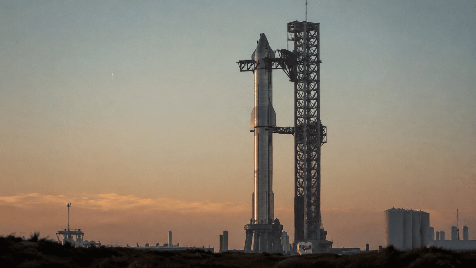 A silver rocket standing on a launchpad at dawn beneath a wide open sky.
