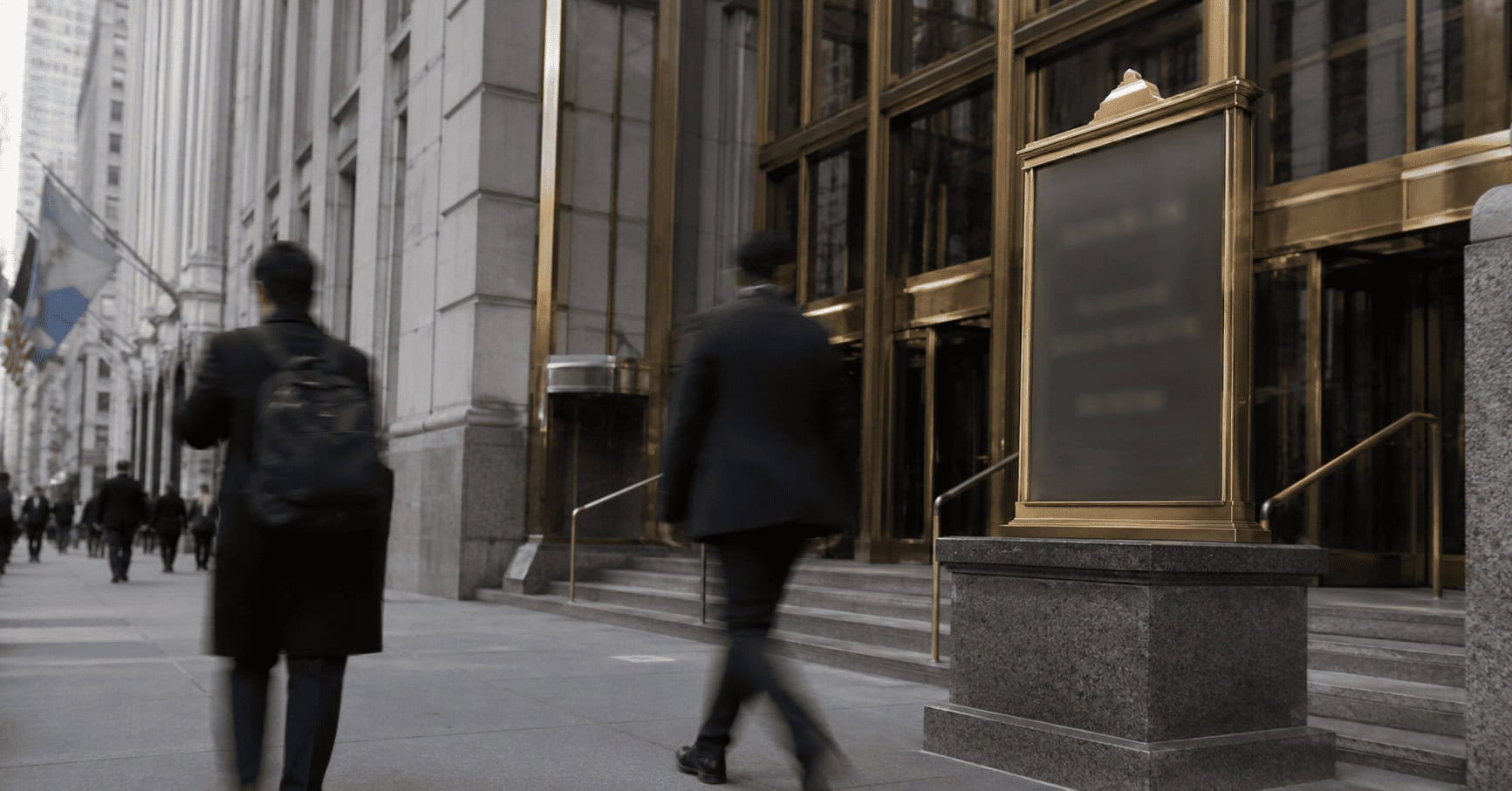 Exterior entrance of a Wall Street bank headquarters with pedestrians walking past on an overcast day.