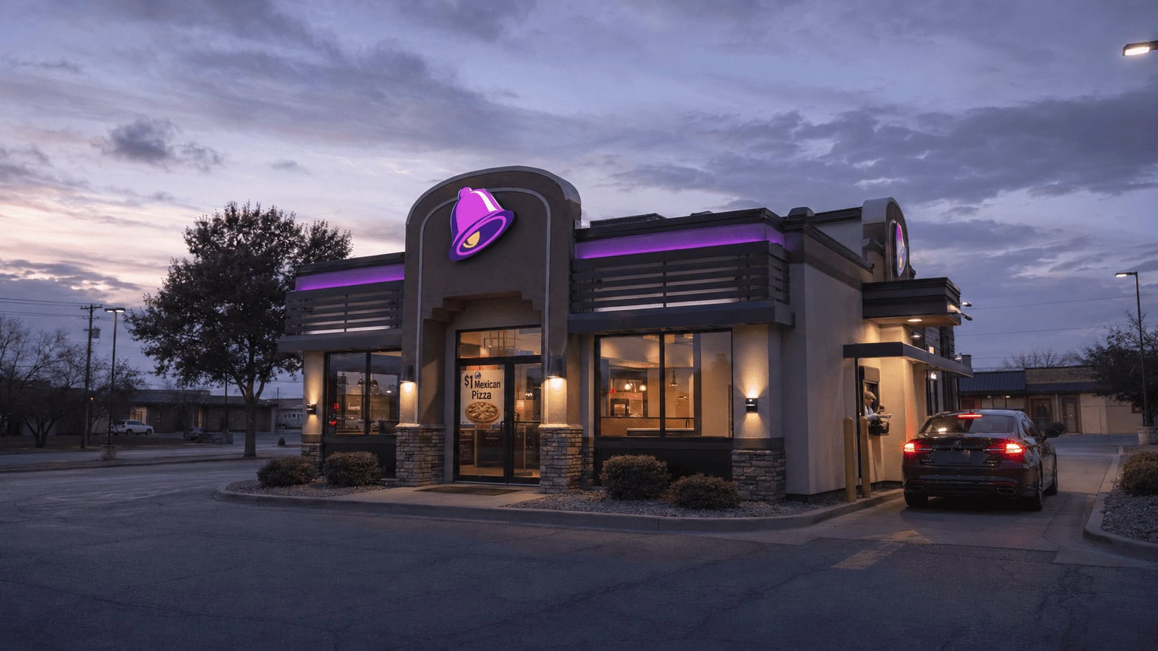 Taco Bell drive-thru at dusk with a $1 Mexican Pizza promotion banner.
