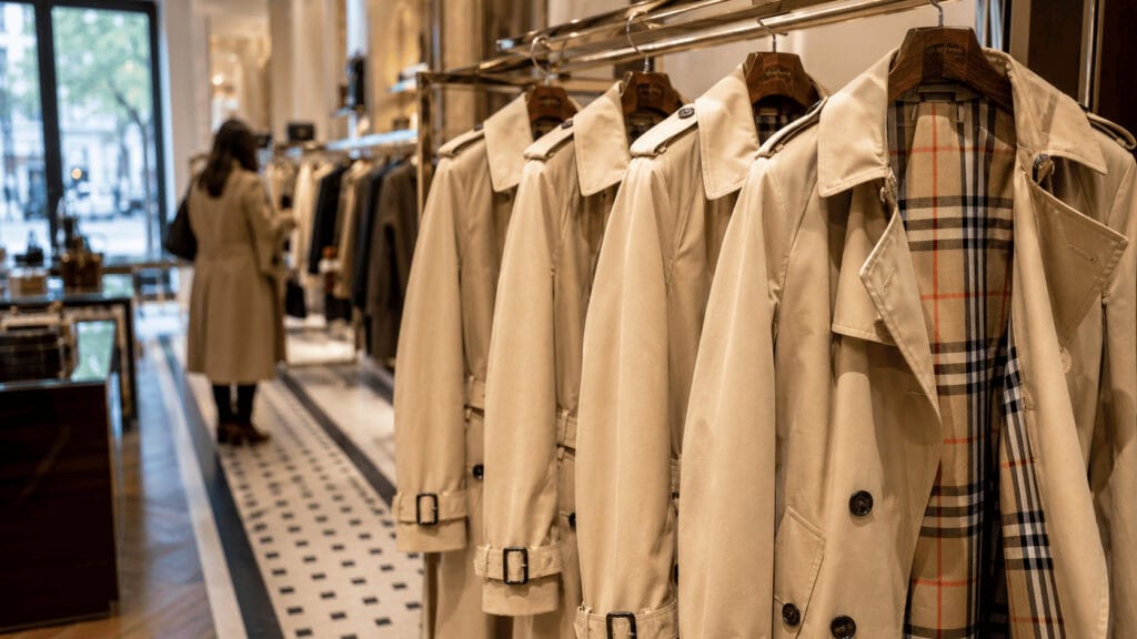 Beige Burberry trench coats with signature check lining displayed in a luxury flagship store.