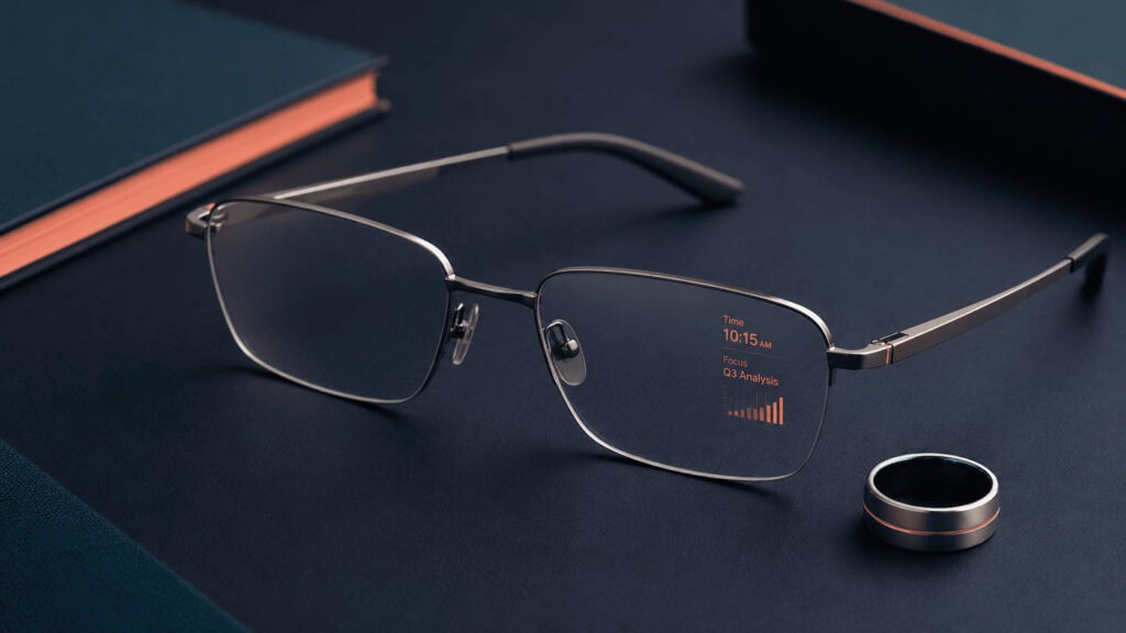A pair of thin, camera-free smart glasses with a faint amber heads-up display glow, shown beside a slim metal control ring on a matte navy surface, illustrating Even Realities' premium display-first design.
