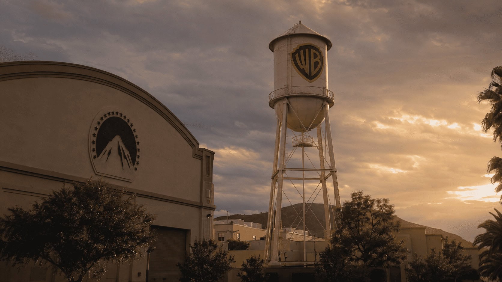 Warner Bros. studio water tower beside a Paramount Pictures soundstage, illustrating Paramount's $81 billion EU-approved acquisition of Warner Bros. Discovery.