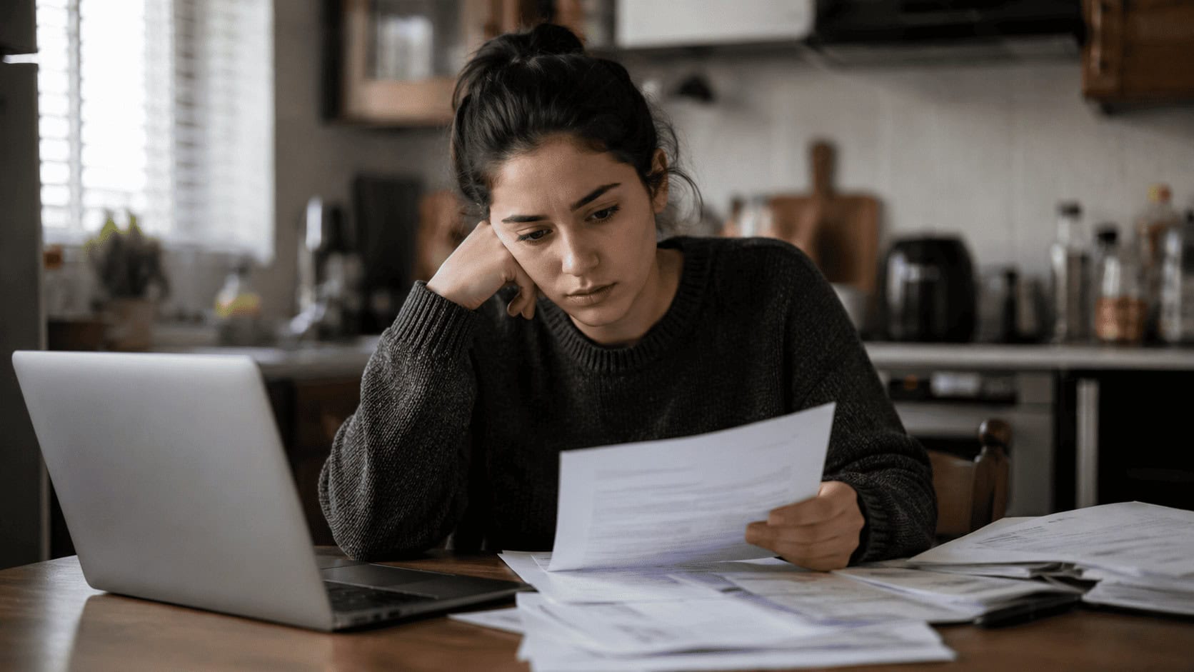 A young borrower reviews federal student loan statements at a kitchen table beside a laptop after the 2026 repayment rule changes.