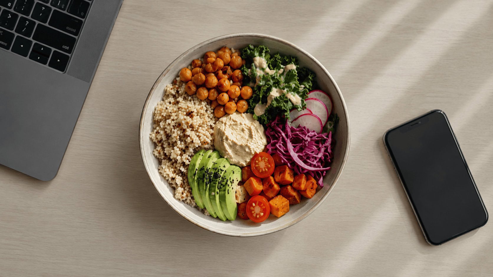 A Sweetgreen grain bowl on an office desk beside a laptop, illustrating the urban weekday lunch occasion that defines Sweetgreen's target market.
