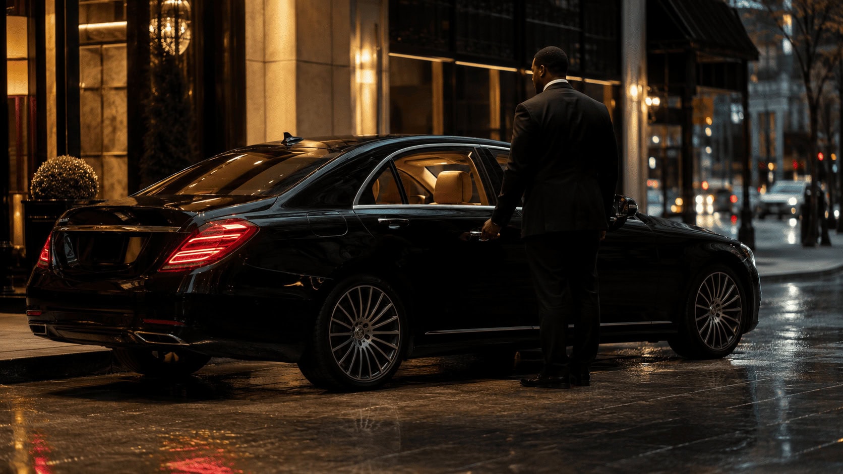 Wheely chauffeur in a dark suit standing beside an unmarked black luxury car outside a New York City hotel at dusk
