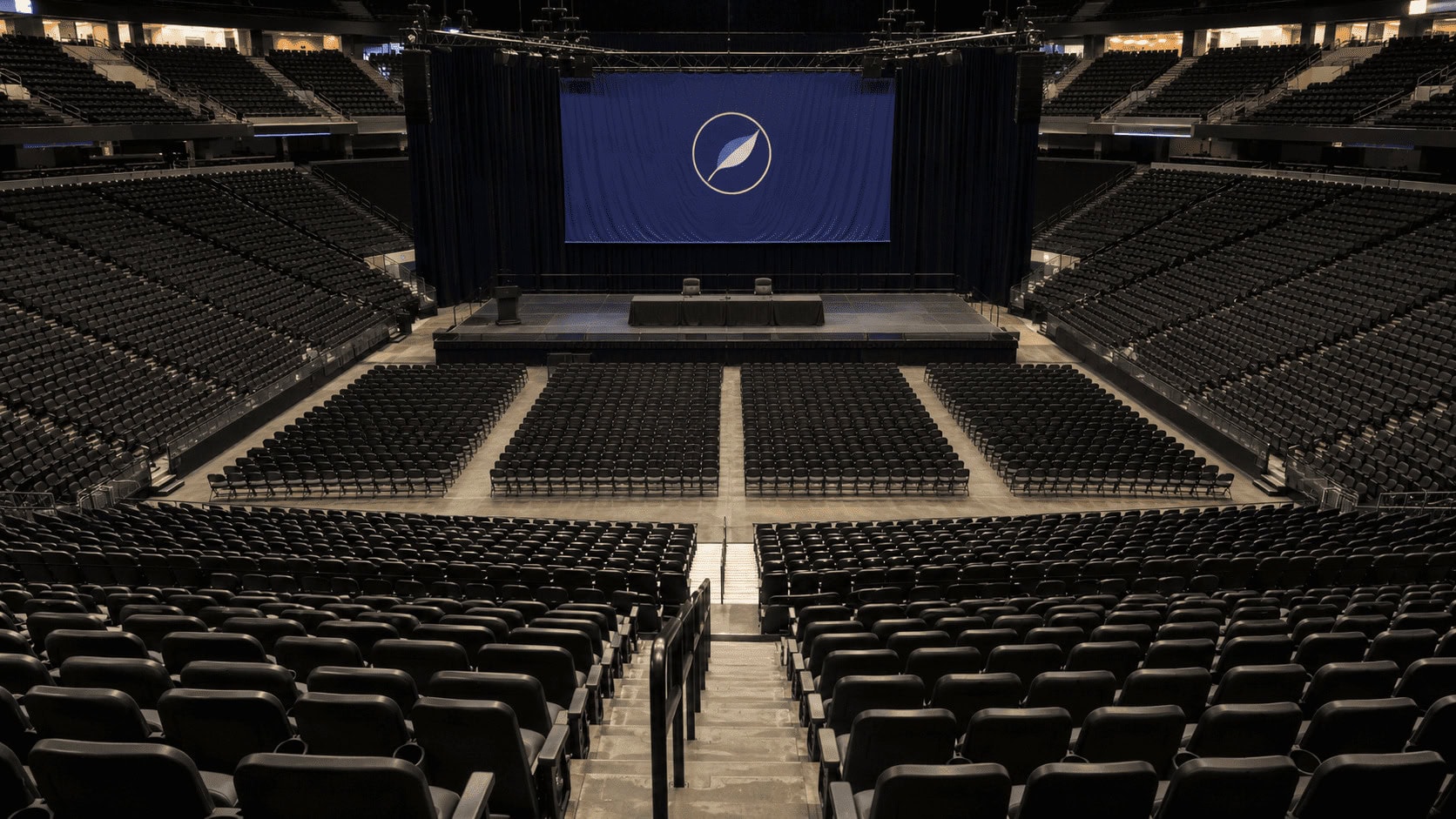 Wide interior shot of the Berkshire Hathaway annual shareholders meeting arena in Omaha with Berkshire Hathaway signage above an empty stage
