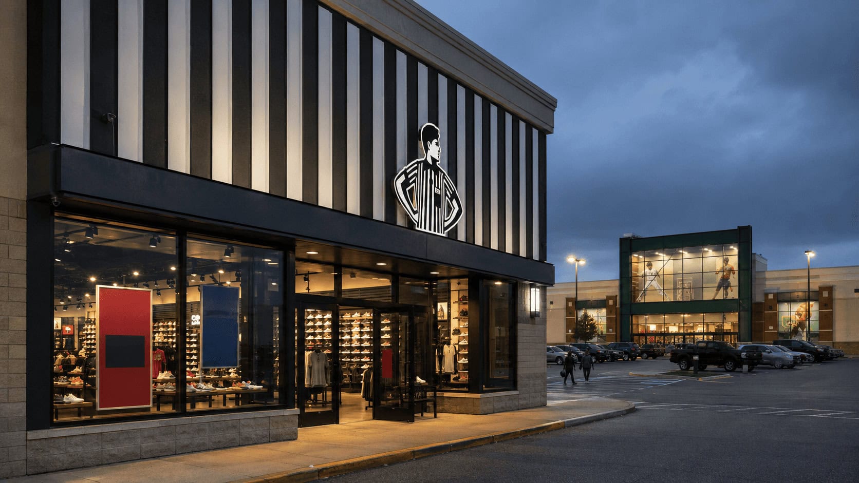 A Foot Locker storefront with promotional window signage, with a Dick's Sporting Goods store visible in the background