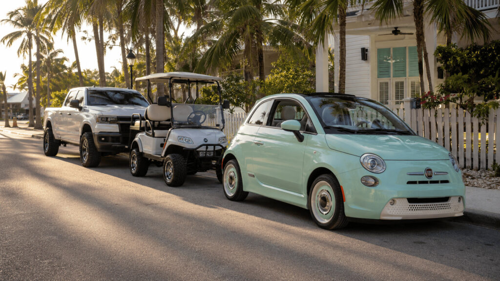 Fiat Topolino microcar parked ahead of a golf cart and a pickup truck on a beach-town street