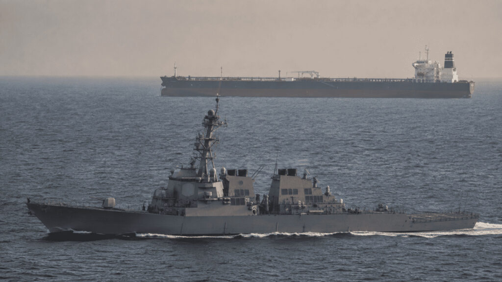 A US Navy destroyer patrolling shipping lanes near an oil tanker in the Persian Gulf at dusk