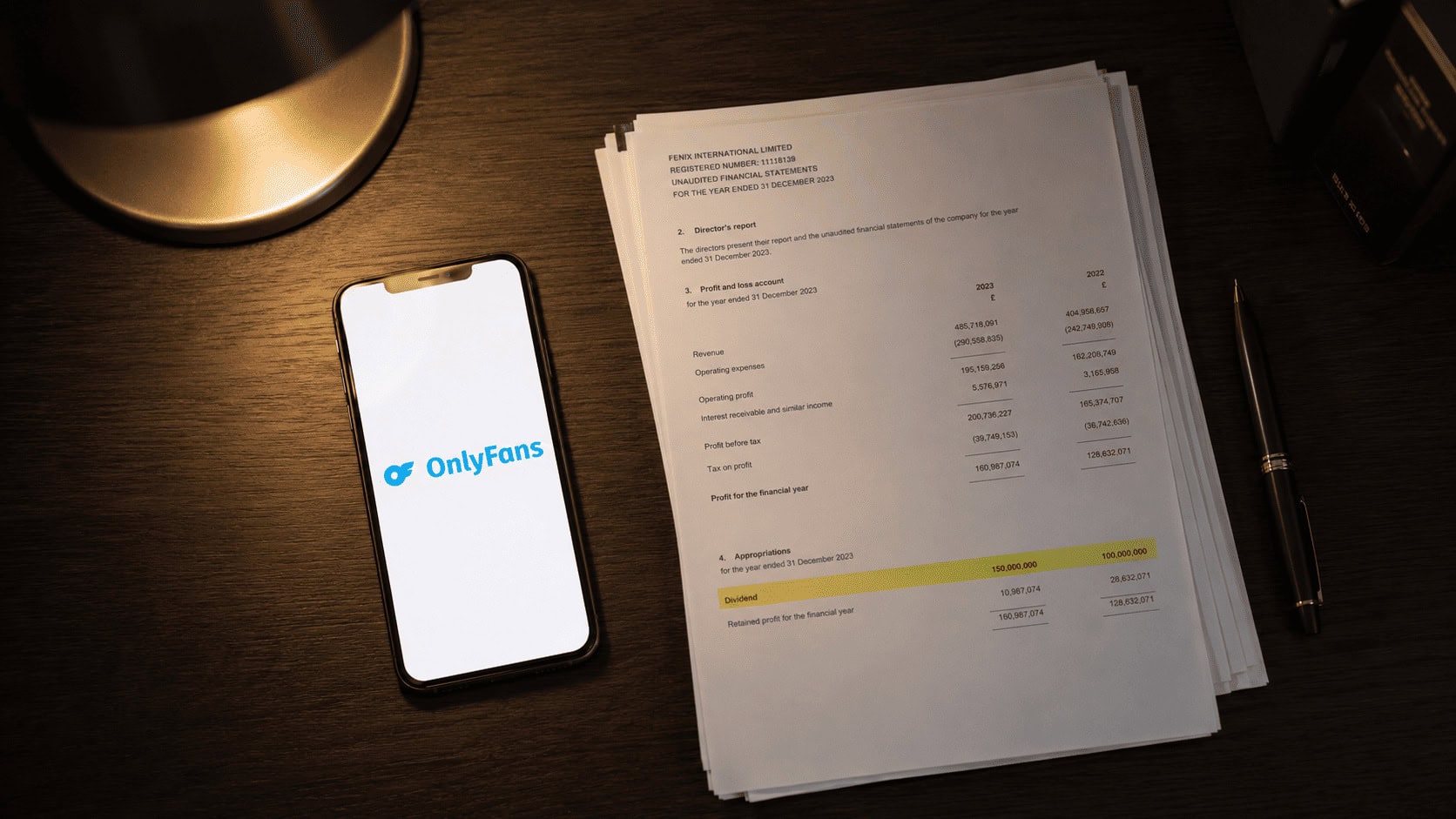 OnlyFans logo glowing on a smartphone screen beside a printed financial statement on a dark desk