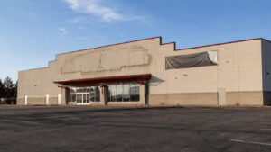 An empty single-tenant retail building with a vacant pylon sign and a fresh For Lease banner in a suburban parking lot at dusk