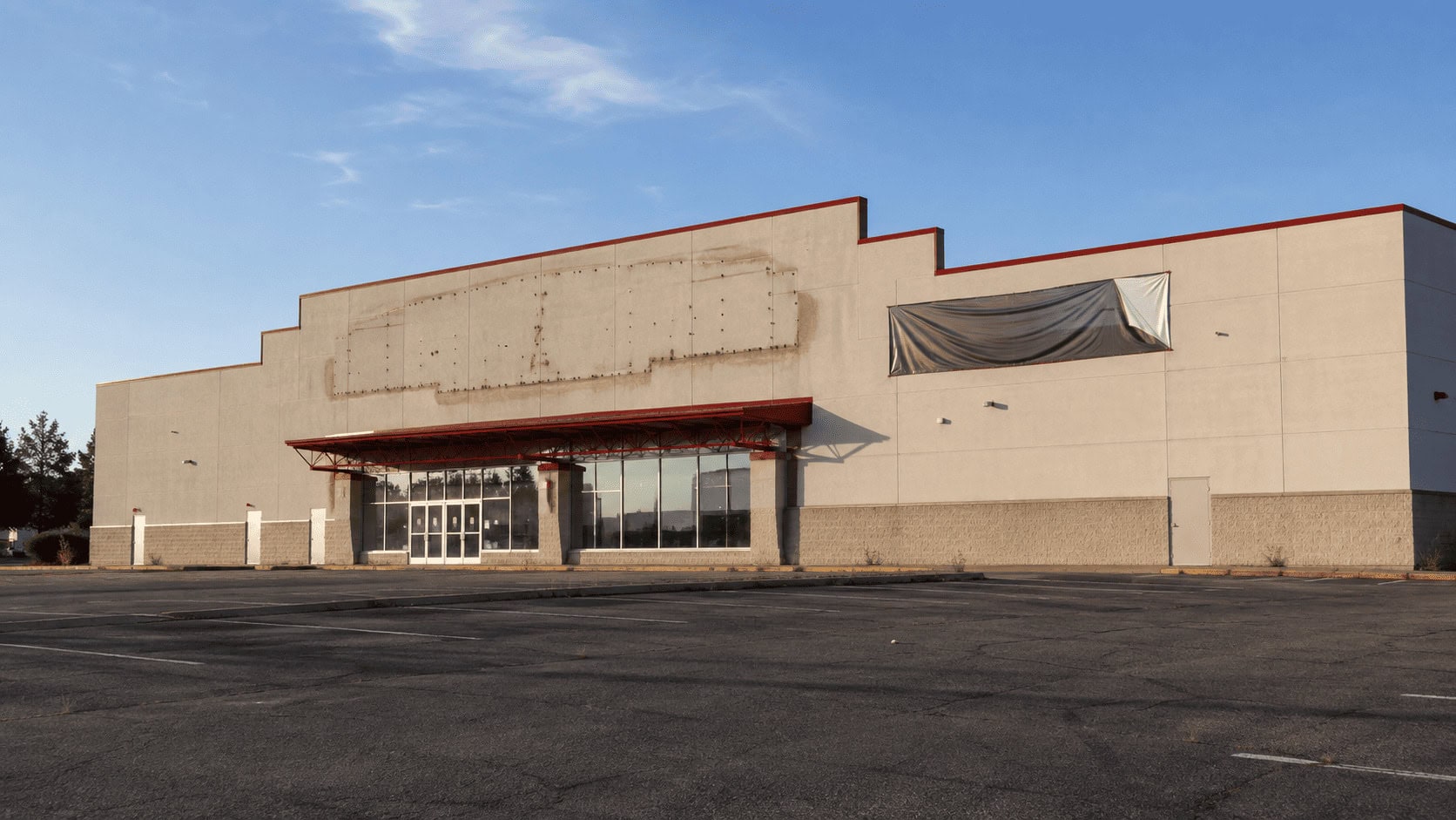 An empty single-tenant retail building with a vacant pylon sign and a fresh For Lease banner in a suburban parking lot at dusk