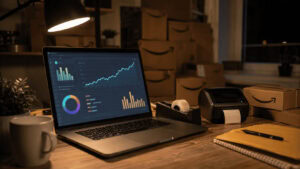 A small e-commerce seller's desk at night with a laptop showing a rising advertising cost dashboard beside stacked Amazon shipping boxes