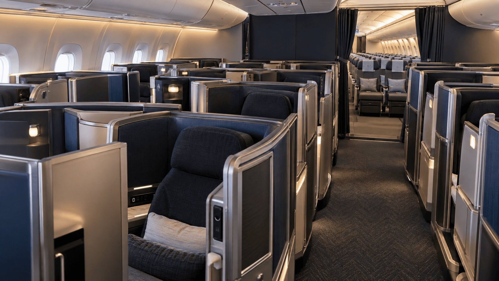Cabina de un Boeing 777 de American Airlines con filas de suites cerradas de clase ejecutiva y asientos de clase económica premium detrás de un separador