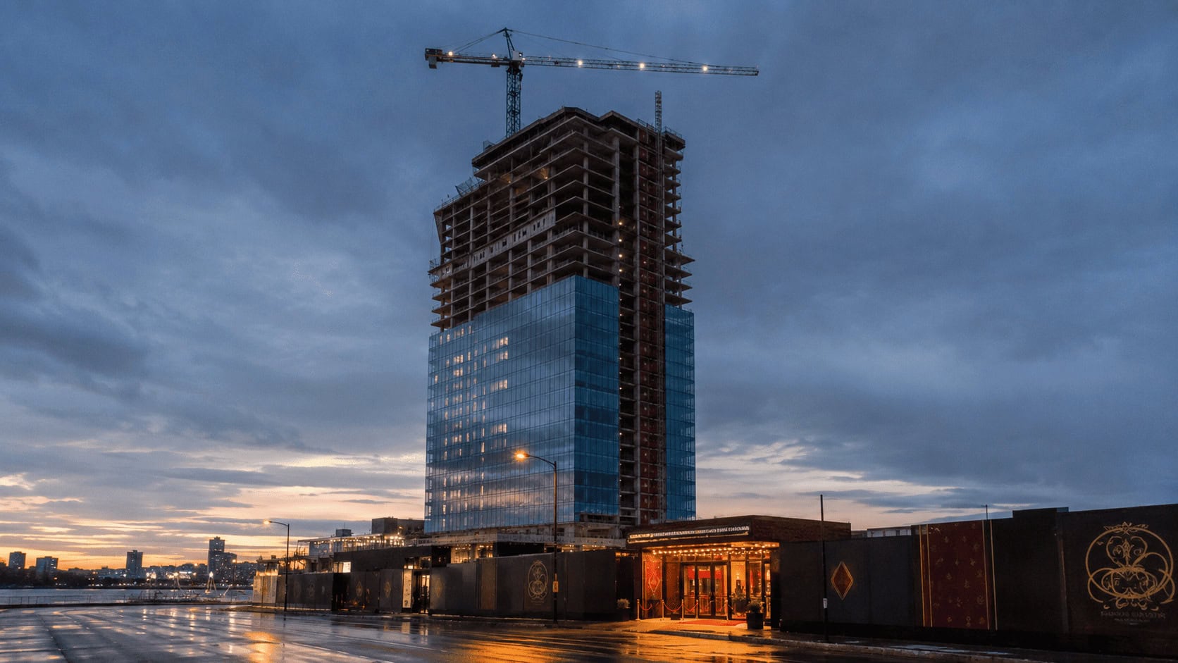 Unfinished casino resort tower and an idle construction crane on a city riverfront at dusk