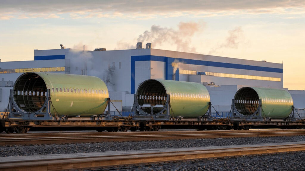 Green-primer Boeing 737 fuselage sections strapped to a rail flatcar leaving the Wichita plant at dawn